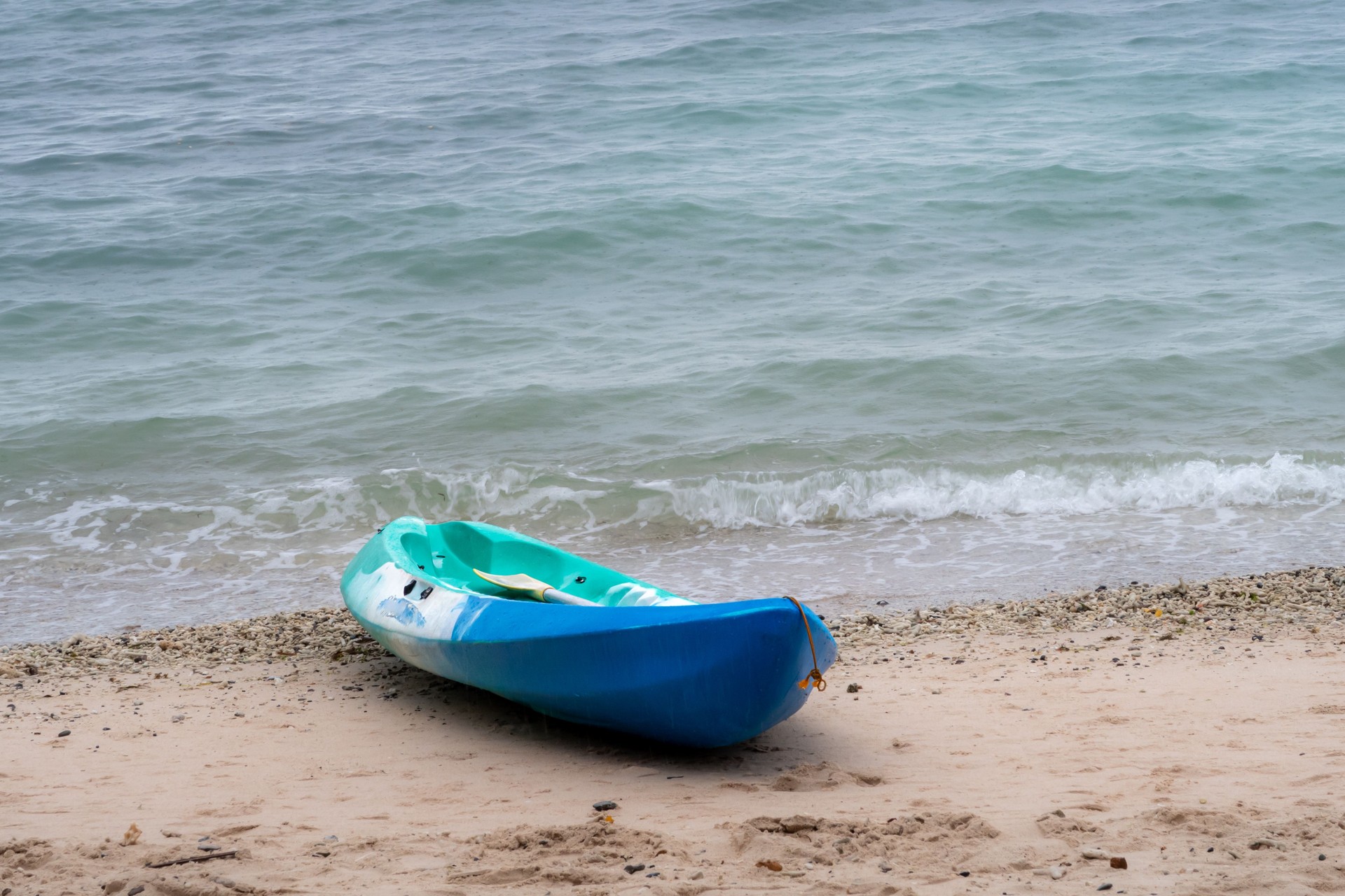 A blue and green kayak on a tropical sandy beach with the emerald green sea in the background